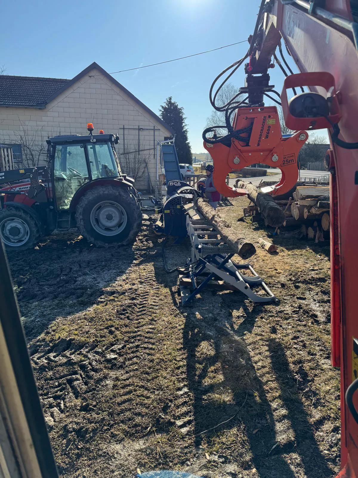 Ein großer und ein kleiner Traktor stehen in einem Hof, neben dem SÄGESPALTER RCA 400 JOY.